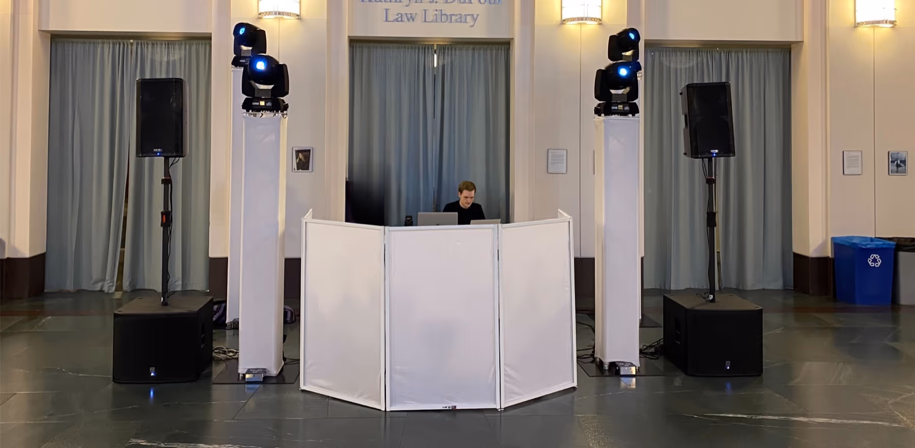 DJ booth with a white facade between speakers and moving lights in a library hall